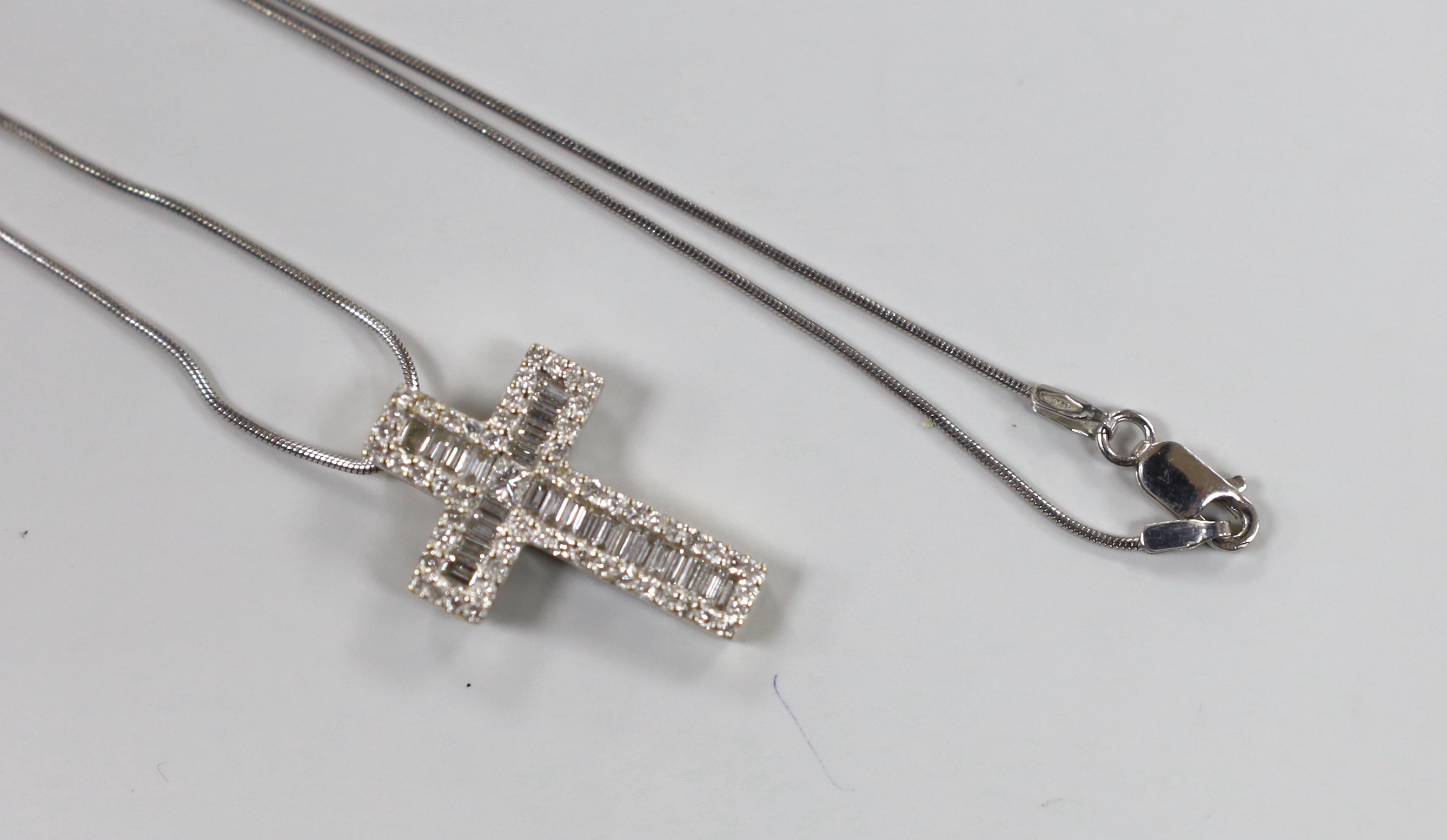 A modern 750 white metal, baguette and round cut diamond cluster set cross pendant, 23mm, gross 3.1 grams, on a 375 white metal fine chain, 46cm, 2.6 grams.